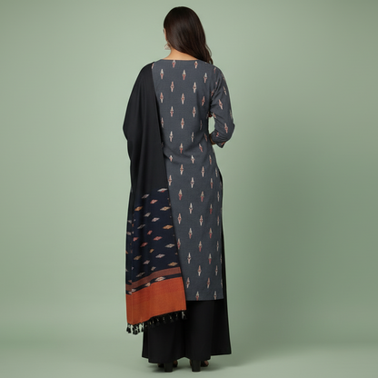 Woman wearing a traditional outfit with a patterned shirt, black dupatta, and wide-leg pants on a green background