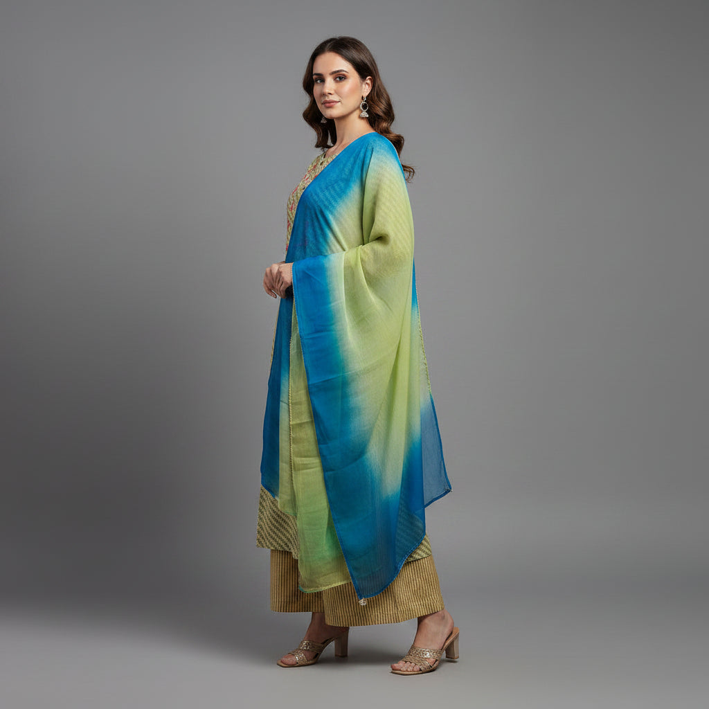 A woman modeling a traditional Indian outfit consisting of a light olive green kurta with gold stripes, matching brown pants, and a blue-green gradient dupatta, set against a solid gray studio background.