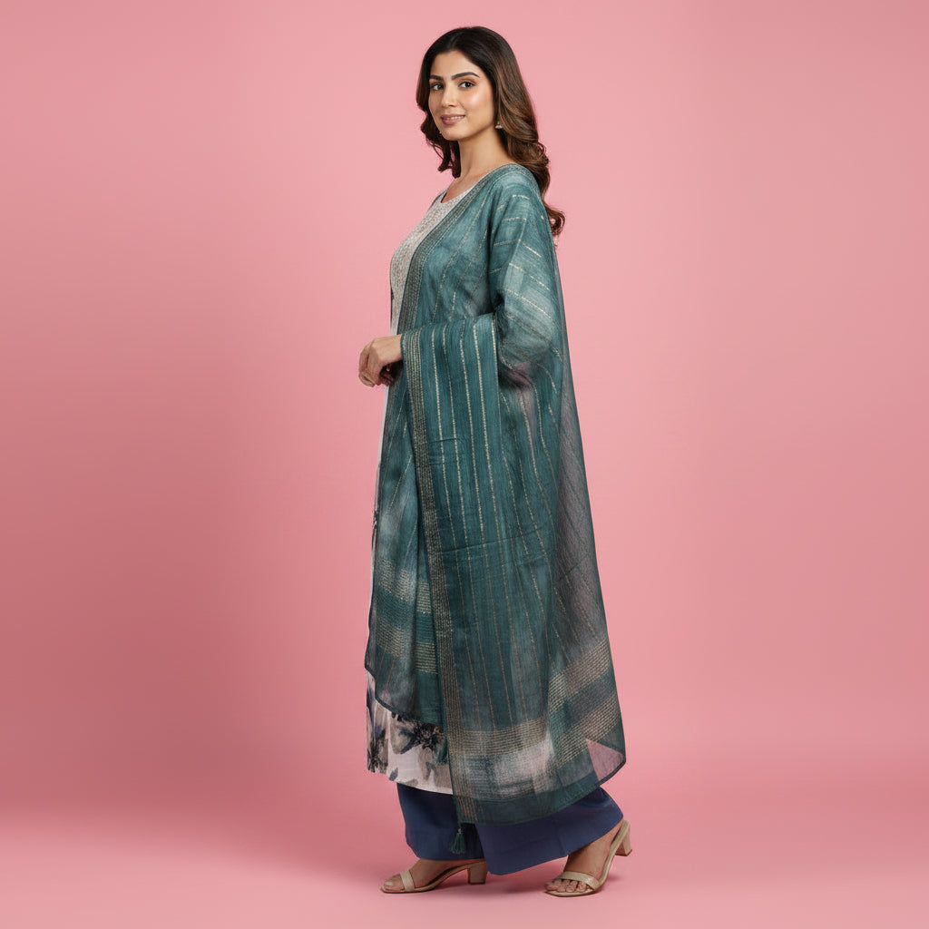 A woman modeling a traditional Indian outfit consisting of a long-sleeved kurta with a white, gray, and blue floral print, a matching teal-green shawl draped over her shoulders, and navy blue pants, set against a solid pink studio background.
