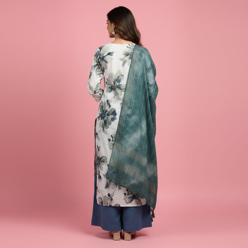 A woman modeling a traditional Indian outfit consisting of a long-sleeved kurta with a white, gray, and blue floral print, a matching teal-green shawl draped over her shoulders, and navy blue pants, set against a solid pink studio background.