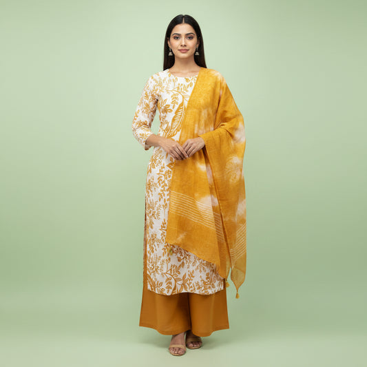 A woman shown from the back wearing a white kurta with a gold floral pattern, a mustard yellow shawl with white tie-dye, and mustard yellow pants, set against a solid pale green studio background.