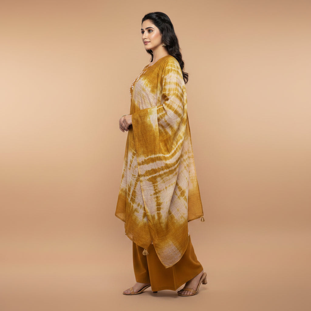 A woman modeling a mustard yellow and white tie-dye salwar kameez suit with matching pants and dupatta against a plain white background.