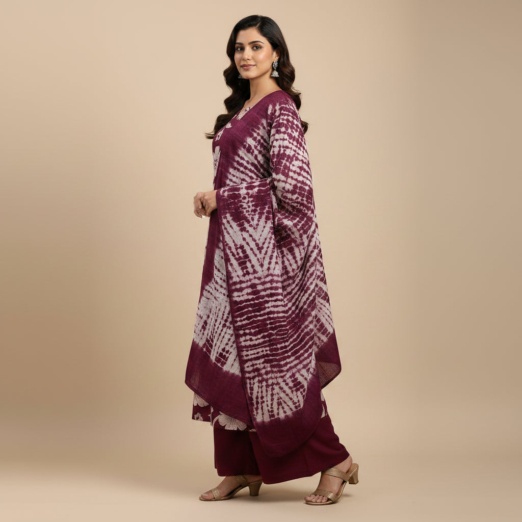 A woman modeling a deep purple and white floral printed kurta set with matching pants and dupatta against a solid beige studio background.