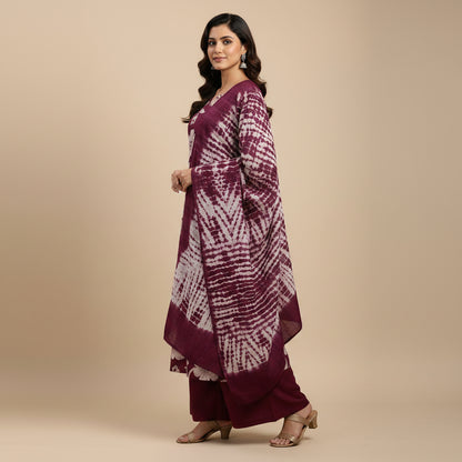 A woman modeling a deep purple and white floral printed kurta set with matching pants and dupatta against a solid beige studio background.