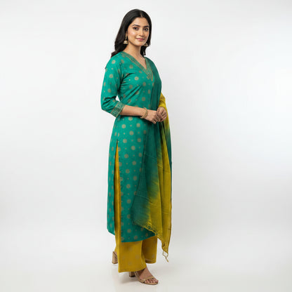 A woman modeling a traditional Indian outfit consisting of a teal green kurta with gold polka dots, matching trousers, and a matching gradient green and yellow dupatta, set against a plain white studio background.