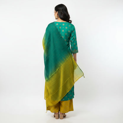 A woman modeling a traditional Indian outfit consisting of a teal green kurta with gold polka dots, matching trousers, and a matching gradient green and yellow dupatta, set against a plain white studio background.