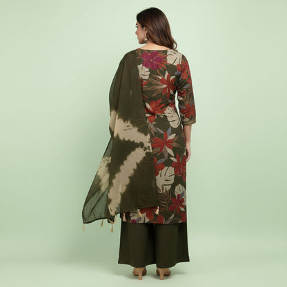 A woman models a three-piece Indian ethnic salwar kameez suit set. The set features an olive green kurta with a red and beige floral print, matching olive green wide-leg trousers, and a matching olive green dupatta with beige tie-dye patterns.