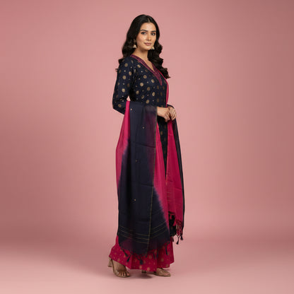 A woman modeling a traditional Indian outfit consisting of a navy blue kurta with gold polka dots, matching navy and pink wide-leg pants, and a vibrant pink and navy tie-dye dupatta, set against a plain light gray studio background.