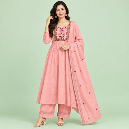 A pink salwar suit set laid flat on a patterned floor, featuring a long-sleeve kurta with floral embroidery around the neckline, matching trousers, and a coordinating dupatta.