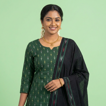 A folded Indian ethnic wear fabric set laid out on a bed, including a green patterned dupatta, a black kurta, and a black palazzo pant, with yellow labels identifying each piece.